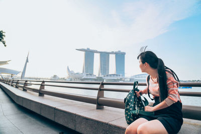 Side view of woman sitting on railing against sky
