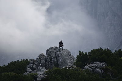 Man on rock by mountain against sky