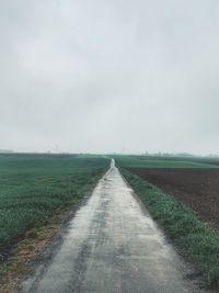 Empty road amidst field against sky