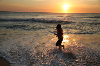 Side view of woman running in sea against sky during sunset