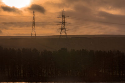 Silhouette electricity pylon on field against dramatic sky