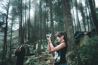 Side view of young woman photographing in forest