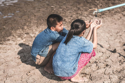 Siblings crouching by tap on drought field