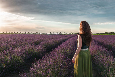 Rear view of woman walking on field against sky during sunset