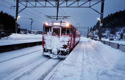 Train on snow covered railroad track against sky during winter
