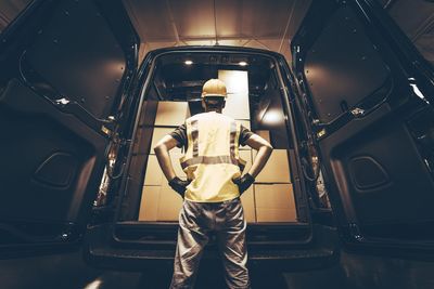 Rear view of delivery person standing by van with cardboard boxes