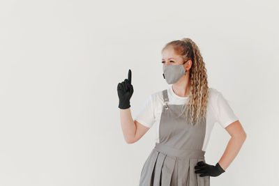 Portrait of young woman wearing mask while standing against white background