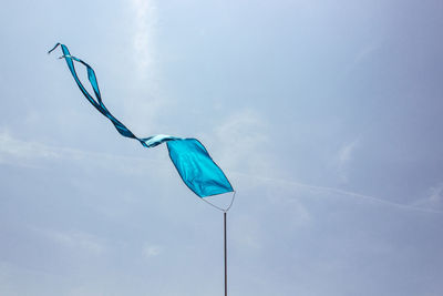 Low angle view of blue textile waving against sky