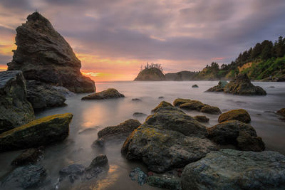 Rocks on sea shore against sky during sunset