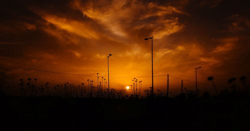 Silhouette street lights against dramatic sky during sunset