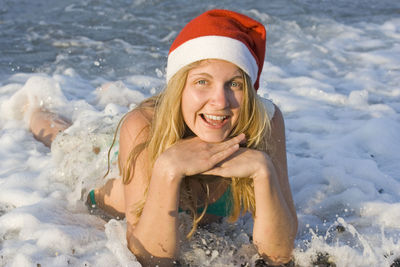 Portrait of happy young woman wearing santa hat lying on beach