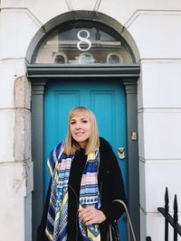 Portrait of smiling woman standing against door