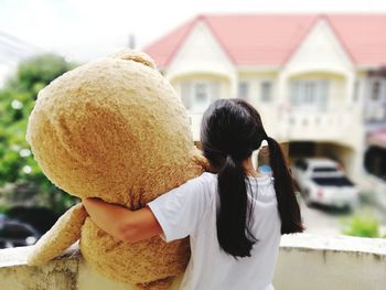 Rear view of woman with toy standing against building