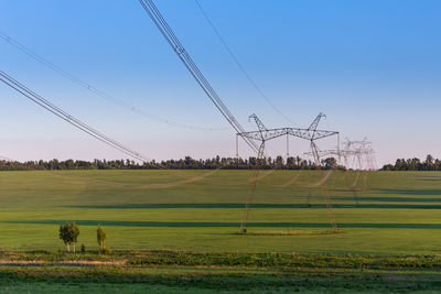 Scenic view of power line towers on green summer field against sky at day light