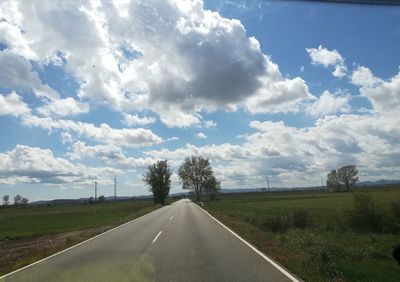 Empty road amidst field against sky