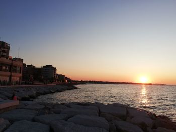 Sea by buildings against sky during sunset