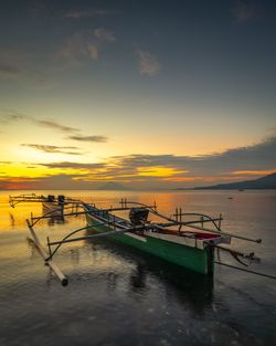 Fishing boat moored in sea against sky during sunset