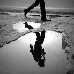 Reflection of man in puddle while walking roadside