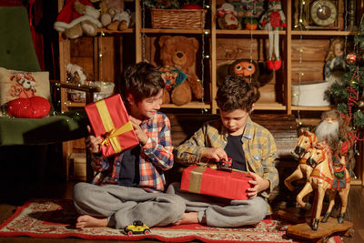 Two real brothers lie in a room with new year's decor near an armchair and look at gifts