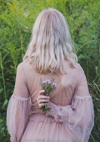 Rear view of woman holding flower while standing against plants