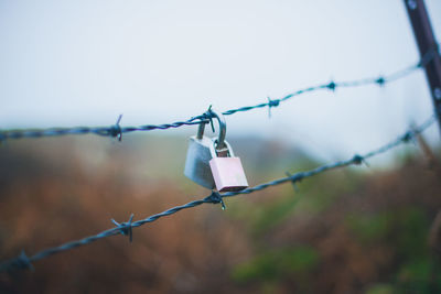 Close-up of padlocks on barbed wire against sky