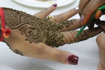 Cropped hand of beautician making henna tattoo on woman hand