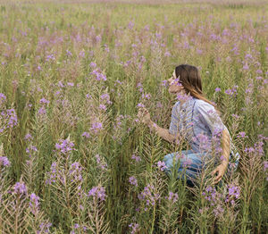 Beautiful blond young woman on field of fireweed flowers sniffing scent flower enjoing nature
