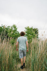 Rear view of man walking on field against sky