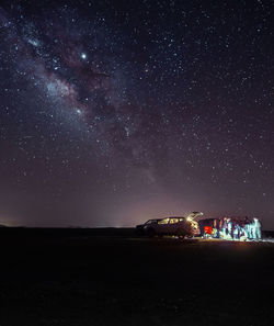 People standing by cars on field against sky at night