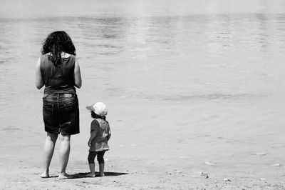 Rear view of mother standing with son on shore at beach