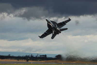 Low angle view of fighter plane flying against cloudy sky