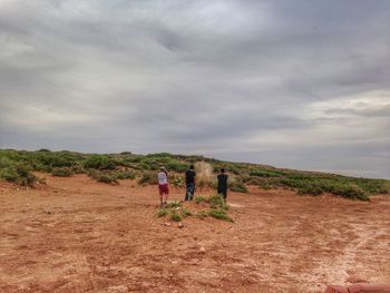 Rear view of friends standing on field against sky