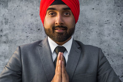 Portrait of smiling businessman wearing turban with clasped hands against wall