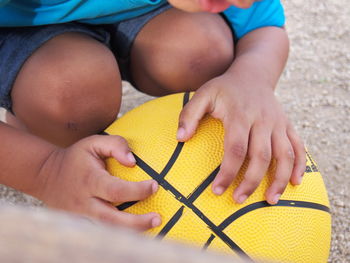 Midsection of boy crouching with yellow basketball on field