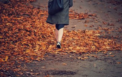 Low section of woman standing on autumn leaves