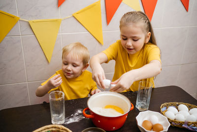 Girl breaks an egg into dough, brother helps cook, easter holiday