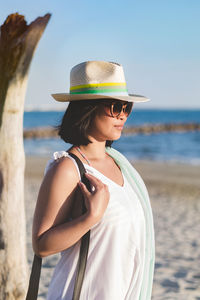 Young woman wearing hat while standing on beach against clear sky