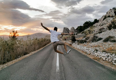 Rear view of man jumping in middle of open road. sumer, wanderlust, travel.