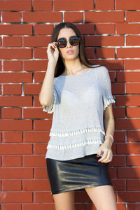 Portrait of a young woman standing against brick wall