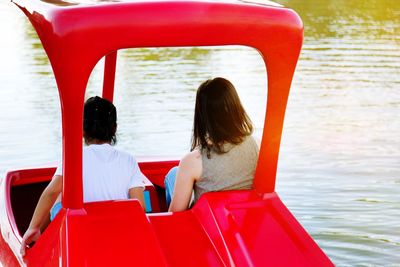 Rear view of girl and woman sitting in pedal boat on lake