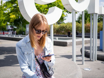 Portrait of young woman using mobile phone while standing in city