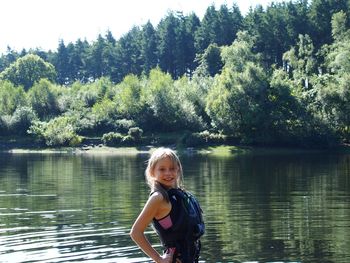 Portrait of girl in life jacket while standing against lake