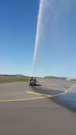 Fire engine splashing water on road against blue sky