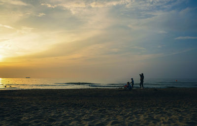 People on beach against sky during sunset