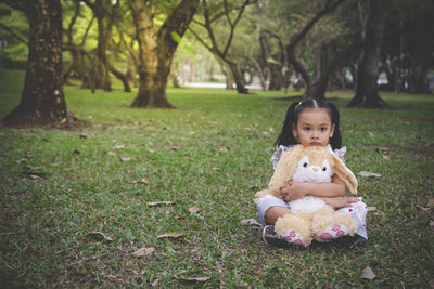 Portrait of innocent girl sitting with stuffed toy at park