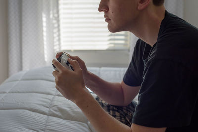 Midsection of man playing video game while sitting on bed