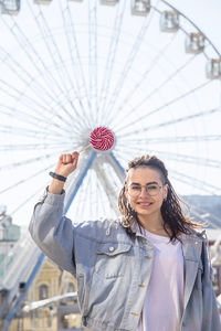 Portrait of smiling young woman holding lollipop with ferries wheel background