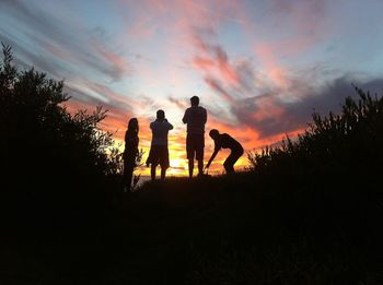 Silhouette of friends against cloudy sky