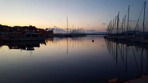 Sailboats moored at harbor against sky during sunset