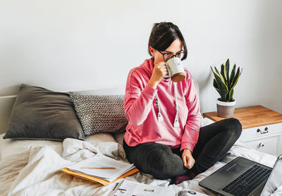 Young woman, student, sitting on bed, studying for exams, laptop, book.